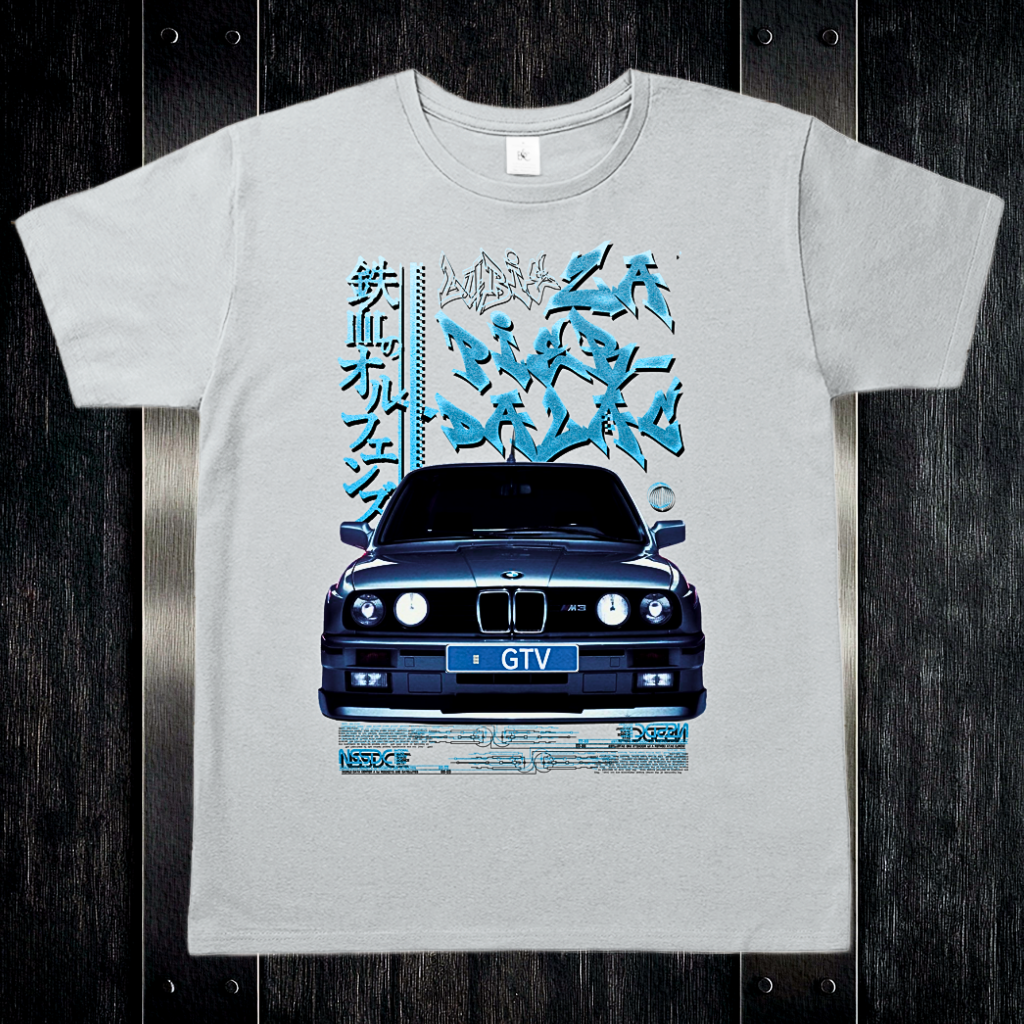 Szara koszulka t-shirt z grafiką BMW E30 w stylu drift glitch na biurku z ciemnego drewna i stalowymi okuciami.