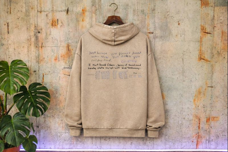 Tył piaskowej bluzy hoodie z dużym nadrukiem listu Kurta Cobaina, efekt sprania vintage washed, stylizowana sesja streetwear.