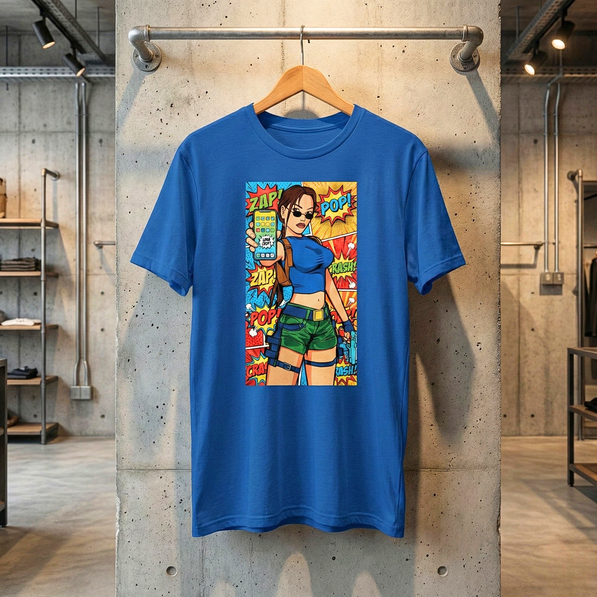 Jasnoniebieska koszulka unisex marki Generate The Vibe zawieszona na drewnianym wieszaku na tle surowego, betonowego filaru. Na froncie t-shirtu znajduje się kolorowy nadruk w stylu pop-art i komiksowym. Grafika przedstawia uzbrojoną postać w okularach przeciwsłonecznych, trzymającą w dłoni smartfon skierowany w stronę widza. Tło nadruku uzupełniają komiksowe onomatopeje, takie jak ZAP!, POP! i CRASH!.
